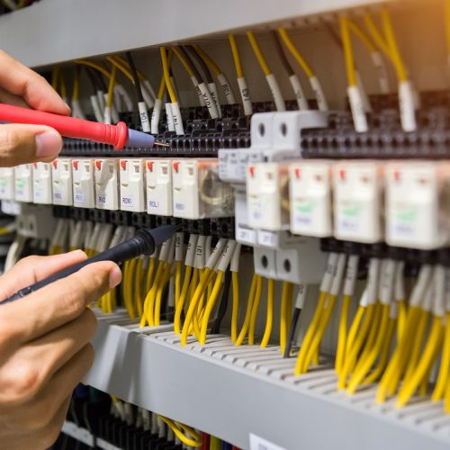 Electricians hands testing current electric in control panel.